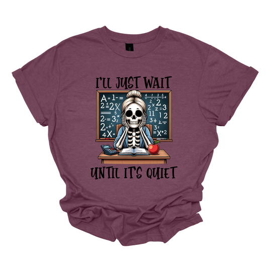 This T-shirt features a skeleton sitting at a cluttered desk, dressed in a cozy cardigan with a messy bun on top of its skull. The skeleton is leaning forward, resting its head on its bony hands as if exhausted or overwhelmed.  The shirt says, "I'll just wait until its quiet".  Shop at Gorgeousware.com 