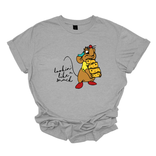 This t-shirt showcases a fun and cheeky design with the playful phrase "Lookin' Like a Snack" written in a delicate black cursive font that adds a touch of elegance. The text is both stylish and sassy, making a light-hearted statement. Adjacent to the text, there's an adorable illustration of the cartoon character Gus Gus from Cinderella. Gus Gus is depicted carrying a blocks of cheese stacked high, balancing it on his chin with a charmingly clumsy look. Shop Gorgeousware.com