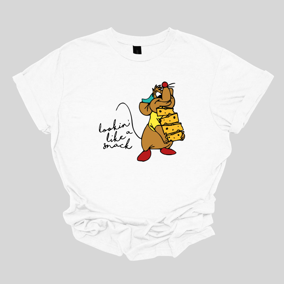 This t-shirt showcases a fun and cheeky design with the playful phrase "Lookin' Like a Snack" written in a delicate black cursive font that adds a touch of elegance. The text is both stylish and sassy, making a light-hearted statement.&nbsp;Adjacent to the text, there's an adorable illustration of the cartoon character Gus Gus from Cinderella. Gus Gus is depicted carrying a blocks of cheese stacked high, balancing it on his chin with a charmingly clumsy look. Shop Gorgeousware.com