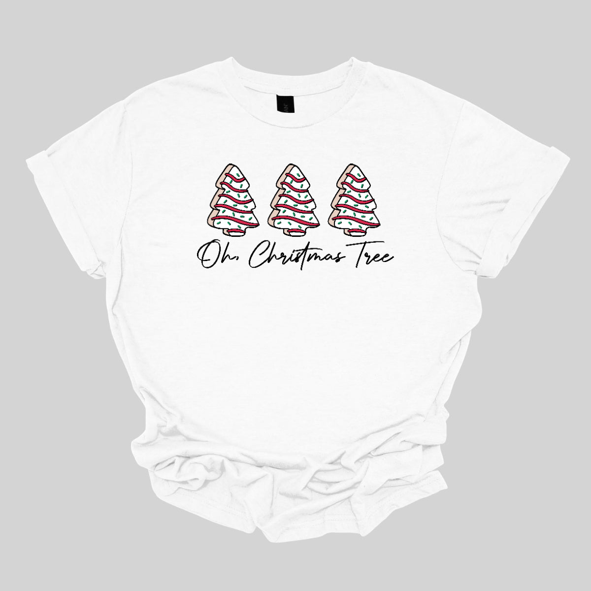 This t-shirt features a whimsical holiday design that’s perfect for spreading cheer. The shirt is adorned with the phrase “Oh Christmas Tree” written in elegant black cursive font, adding a touch of sophistication to the festive message. Above the words, three iconic Christmas tree snack cakes are illustrated, each depicted with their classic, playful decorations. Shop Gorgeousware.com