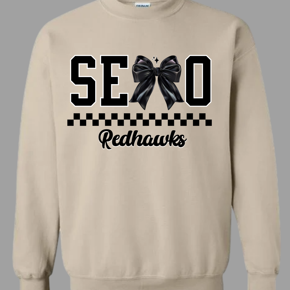 Show off your SEMO pride in style with this trendy creneck and hoodie! Featuring the bold letters "SEMO," where the "M" is cleverly replaced by a stylish black croquette bow, this shirt adds a unique twist to your wardrobe. Underneath, a playful checkerboard stripe adds a fun touch, while "Redhawks" is elegantly written in a cute cursive font, bringing a touch of flair. Shop at Gorgeousware.com