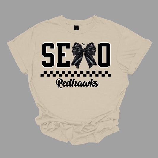 Show off your SEMO pride in style with this trendy short sleeve t-shirt! Featuring the bold letters "SEMO," where the "M" is cleverly replaced by a stylish black croquette bow, this shirt adds a unique twist to your wardrobe. Underneath, a playful checkerboard stripe adds a fun touch, while "Redhawks" is elegantly written in a cute cursive font, bringing a touch of flair. Shop at Gorgeousware.com