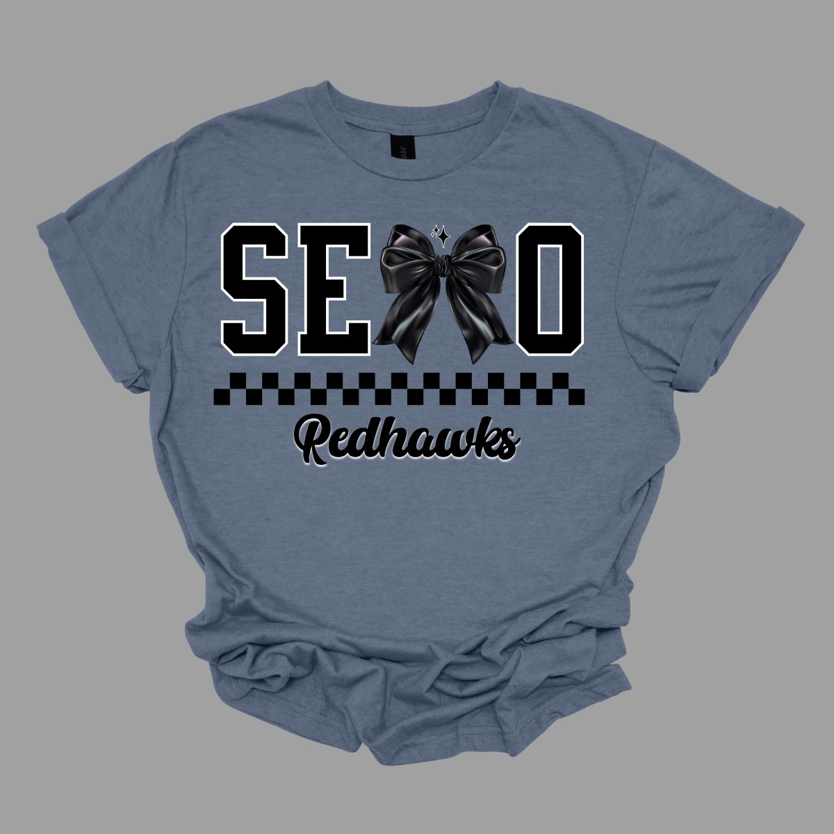 Show off your SEMO pride in style with this trendy short sleeve t-shirt! Featuring the bold letters "SEMO," where the "M" is cleverly replaced by a stylish black croquette bow, this shirt adds a unique twist to your wardrobe. Underneath, a playful checkerboard stripe adds a fun touch, while "Redhawks" is elegantly written in a cute cursive font, bringing a touch of flair. Shop at Gorgeousware.com