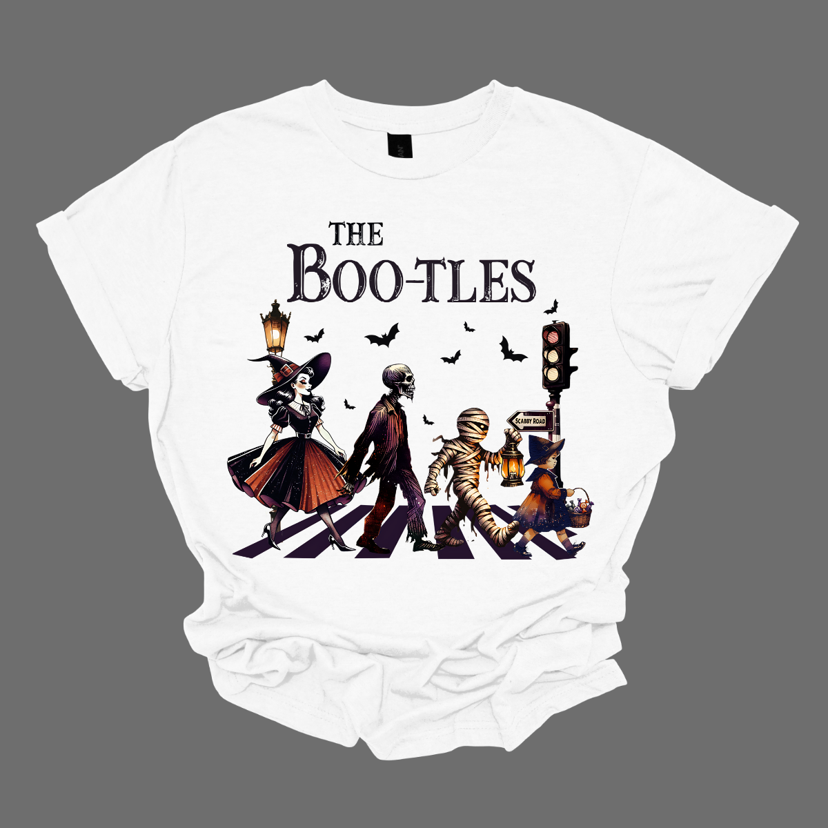 Step into a spooky twist on a classic with our 'Boot-les' tee! This Halloween-themed shirt takes inspiration from the iconic Abbey Road album cover and reimagines it with a creepy-cool lineup of Halloween characters. Picture this: a mischievous witch, a spooky skeleton, a creepy mummy, and a charming little witch, all crossing a spectral road in style.  Shop at Gorgeousware.com