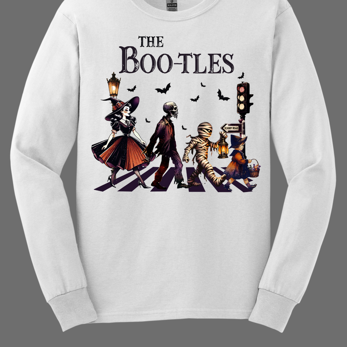 Step into a spooky twist on a classic with our 'Boot-les' tee! This Halloween-themed shirt takes inspiration from the iconic Abbey Road album cover and reimagines it with a creepy-cool lineup of Halloween characters. Picture this: a mischievous witch, a spooky skeleton, a creepy mummy, and a charming little witch, all crossing a spectral road in style.  Shop at Gorgeousware.com